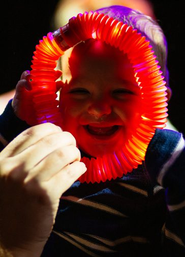 A bearded man holds an illuminated red light ring up to a laughing baby's face.