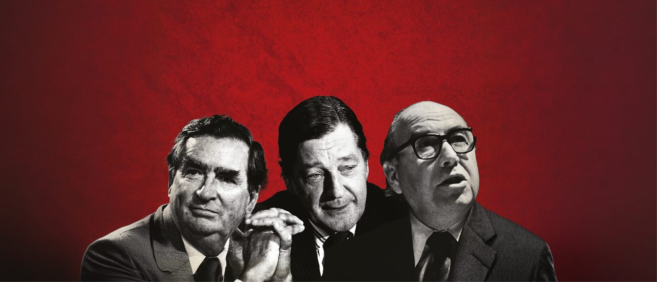 Three men in black and white in front of a red textured background. They are all wearing suits, the man on the right has glasses, is looking off to the right abd has his mouth open slightly. The man in the middle is looking down, a complacent look on his face. The man on the left has his hands clasped together in front of him and looking off to the left.