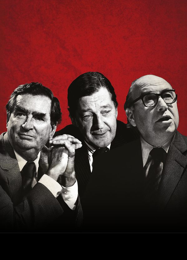 Three men in black and white in front of a red textured background. They are all wearing suits, the man on the right has glasses, is looking off to the right abd has his mouth open slightly. The man in the middle is looking down, a complacent look on his face. The man on the left has his hands clasped together in front of him and looking off to the left.