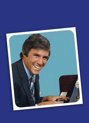 A dark blue background with a tilted photo in the middle. In the photo, is a man in a suit sat at a piano. He is looking at the camera and smiling widely. Behind him is a light blue background with rounded corners and has a white border.