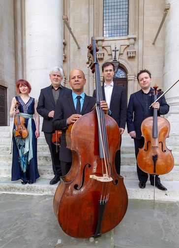 Five musicians holding different string instruments stand on the steps of an impressive sandstone building.
