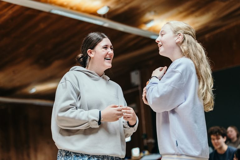 Two young performers laugh together in a rehearsal studio.