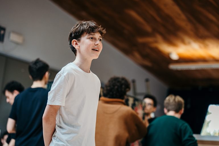 A young performer sings in a rehearsal studio. They are enjoying themselves, looking enthusiastic.