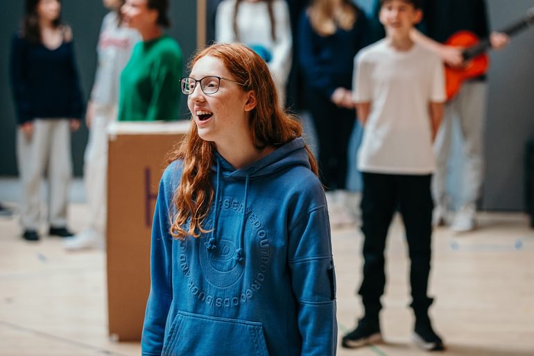 A young performer wearing casual clothes singing in a rehearsal studio. They are happy, enjoying themselves.