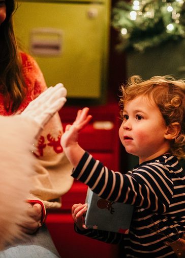 A small child 'high-fives' Santa in a sparkly grotto.