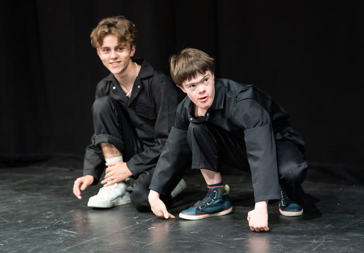 Two CFYT members in black clothes are crouched on the floor, smiling towards the camera
