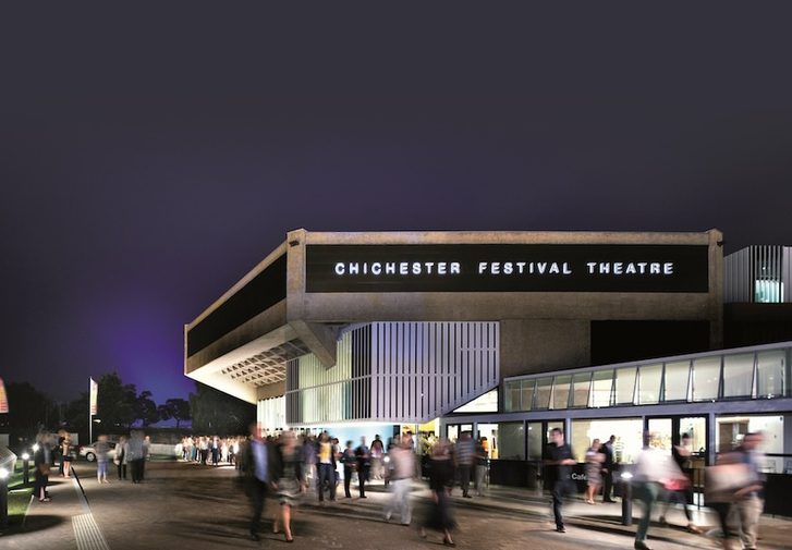 The outside of the Festival Theatre at night time. The building is lit and there is a blur of people moving around outside.