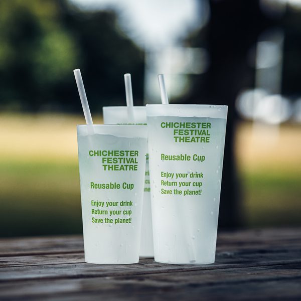 Two of our frosted reusable cups with green writing on the side and green striped paper straws sticking out of them.
