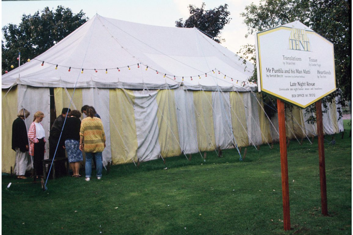 A group gathered at the entrance of a white and yellow tent.