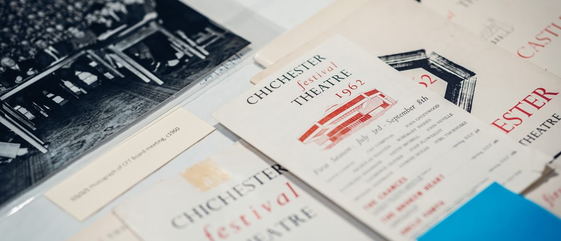 Historic CFT brochures are laid on a surface, with one in the centre labelled '1962'. An old photo of a large crowd of people behind a table can be seen at the top of the frame.