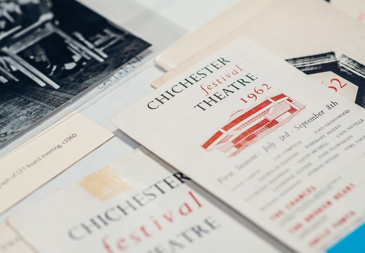 Historic CFT brochures are laid on a surface, with one in the centre labelled '1962'. An old photo of a large crowd of people behind a table can be seen at the top of the frame.