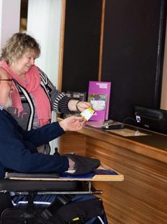 A woman and a man in a wheelchair is speaking with a Box Office assistant.