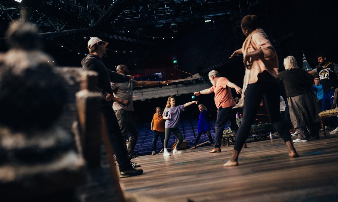 An image taken on stage during warm-up, the actors in casual clothes stretching their arms and legs out.