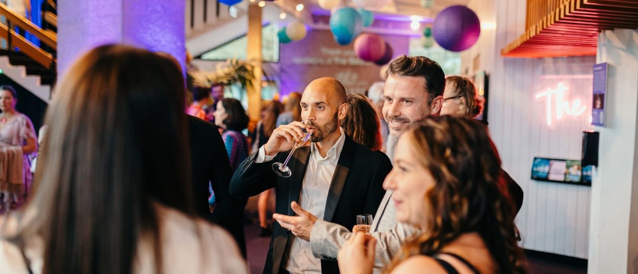 A group of friends smilinh and laughing in the foyer whilst sipping prosecco.