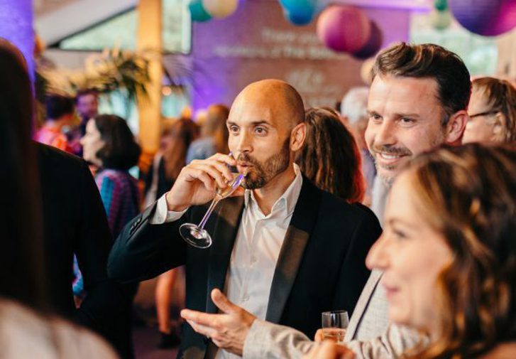 A group of friends smilinh and laughing in the foyer whilst sipping prosecco.