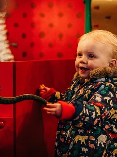 A Child with a happy smiley face watches over to the left of the image as he turns a handle on a red gate.
