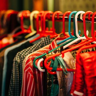 A clothing rack with colourful red, white and green hangars, it holds a row of Santa's clothes. In focus there is a pair of folded red trousers, a stripy red shirt, and a checked green and white shirt.