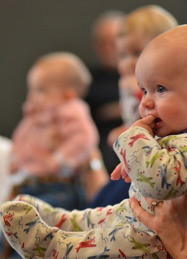 A baby is held up by their parent, with other babies in the background.
