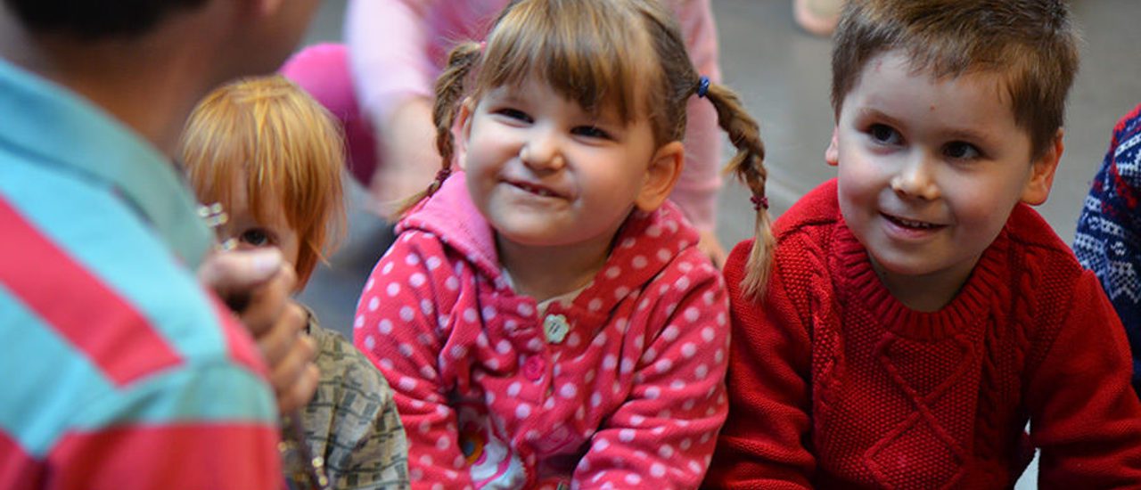 Two young children smile up at a musician.