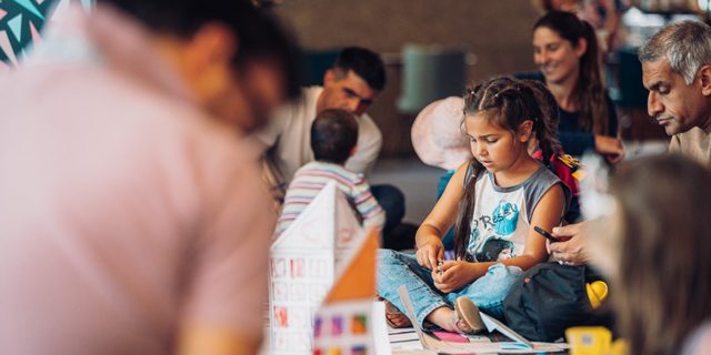 A busy foyer with parents and children sitting together on the floor, chatting and working on crafts.