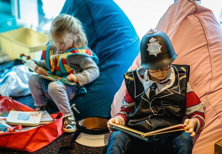 Two children in fancy dress sit on colourful beanbags while busy reading. Books and toys are on the floor around them.