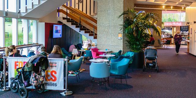 People sitting in chairs and children playing with toys in a wide shot of the pop up family friendly space in the Festival Theatre foyer. l Theatre foyer