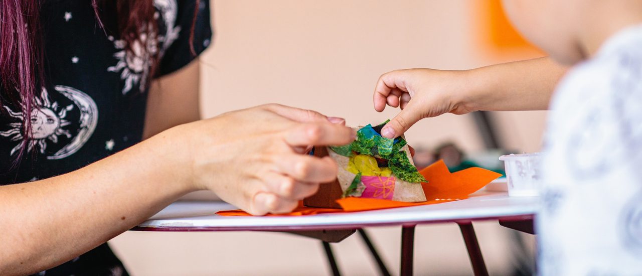 A close up of a woman and boy are sticking a gluing colourful pieces of tissue paper to a model.