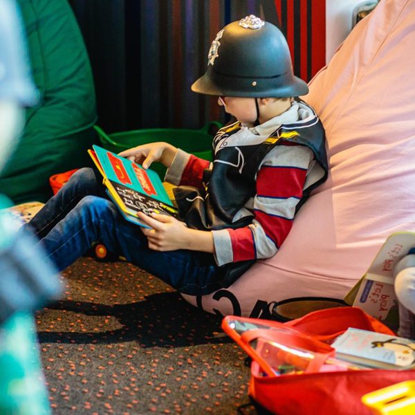 Children in fancy dress outfits and hats sit on beanbags, reading.