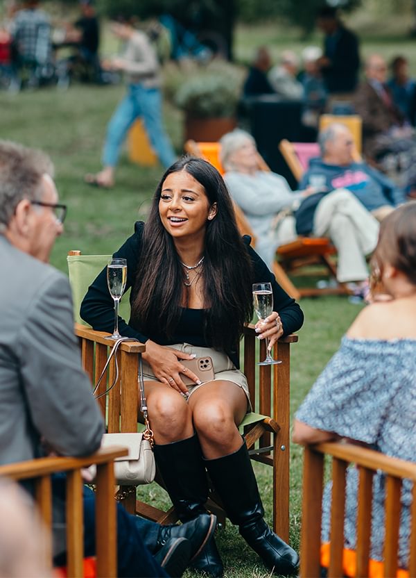 A group of people sit on colourful deckchairs in the park, chatting and smiling.