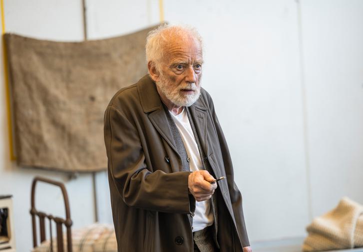 Ian McDiarmid stands in a rehearsal room, with a serious expression on his face. He has wispy white hair and a beard, wears a long brown coat and holds a key in his hand. He is pointing the key out in front of him, as if it might be a weapon.
