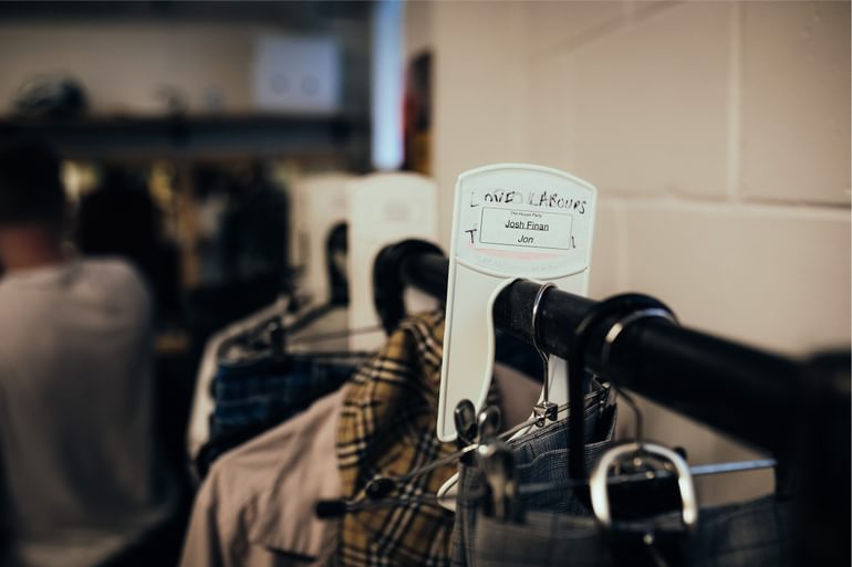 A clothing rail with various hangers and items of costume hanging on it, with a label that reads 'Josh Finan, Jon'.