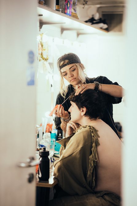 A photo taken from the edge of a door, through the door we can see an actor getting his hair done.