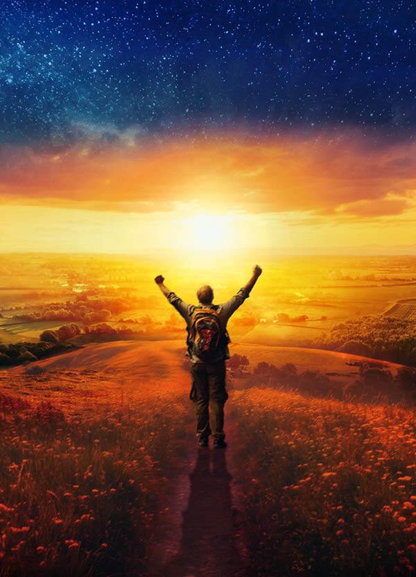 A man stands looking over a wide country landscape, with sunrise illuminating the scenery. Seen from behind, the man's arms are raised in exultation, and he wears a rucksack on his back. A flowery meadow in the foreground slopes away to green fields, woods and distant hills, and the sun is burning away the clouds and remnants of stars; it's an uplifting, rural scene.
