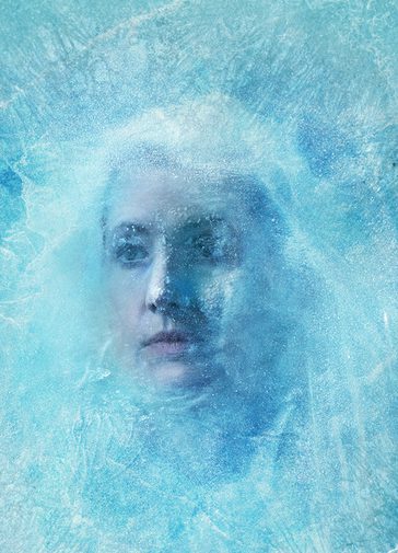 A woman frozen behind a sheet of ice - her hair is pulled out of her face to show her expression, also frozen in time.