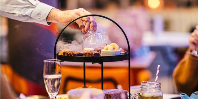A man's hand is revealing a delicious delight on on Afternoon Tea on tiered plates