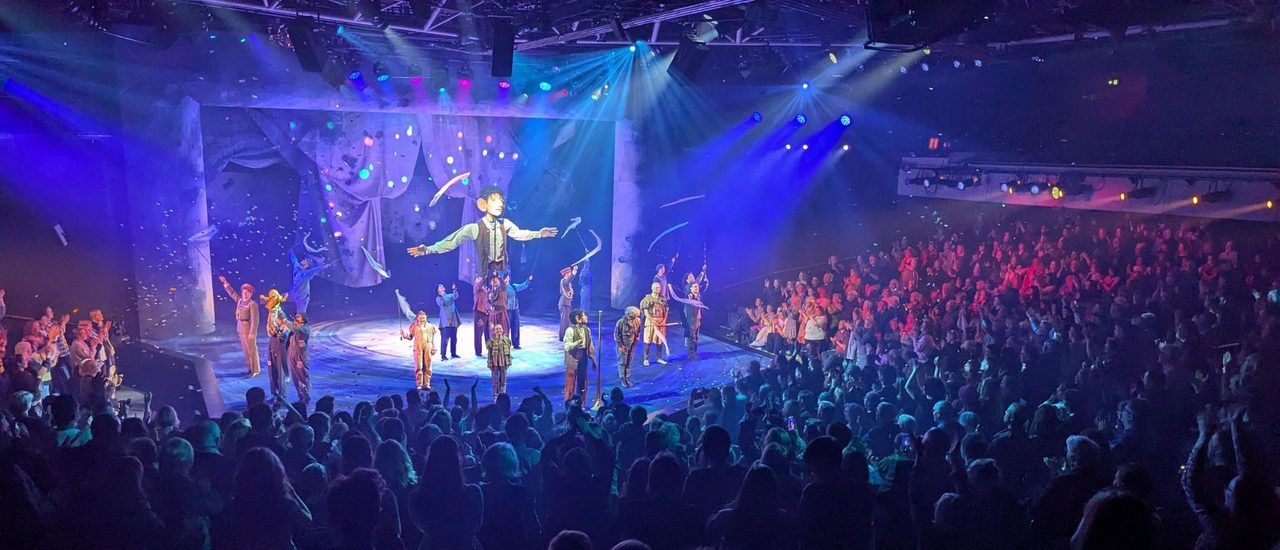 A group of people in casual clothes hold aloft a giant puppet on poles; only the puppet's arms, hands and the lower half of its torso can be seen.