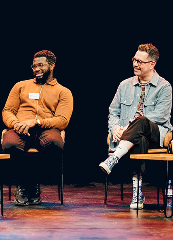 Three men and one woman, of different ages, dressed in casual clothes are sat on our stage holding microphones. One person is talking into the microphone while the others listen