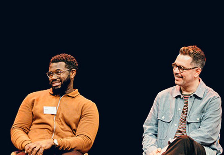 Three men and one woman, of different ages, dressed in casual clothes are sat on our stage holding microphones. One person is talking into the microphone while the others listen