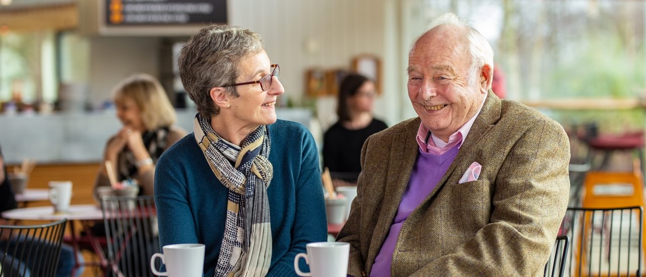 A man and a woman sitting together in our café enjoying a cup of tea and laughing together
