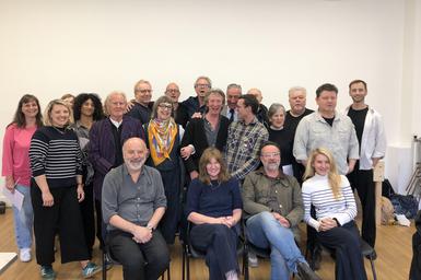 A group of people stand and sit together in a studio. They are all smiling and laughing, having a great time.