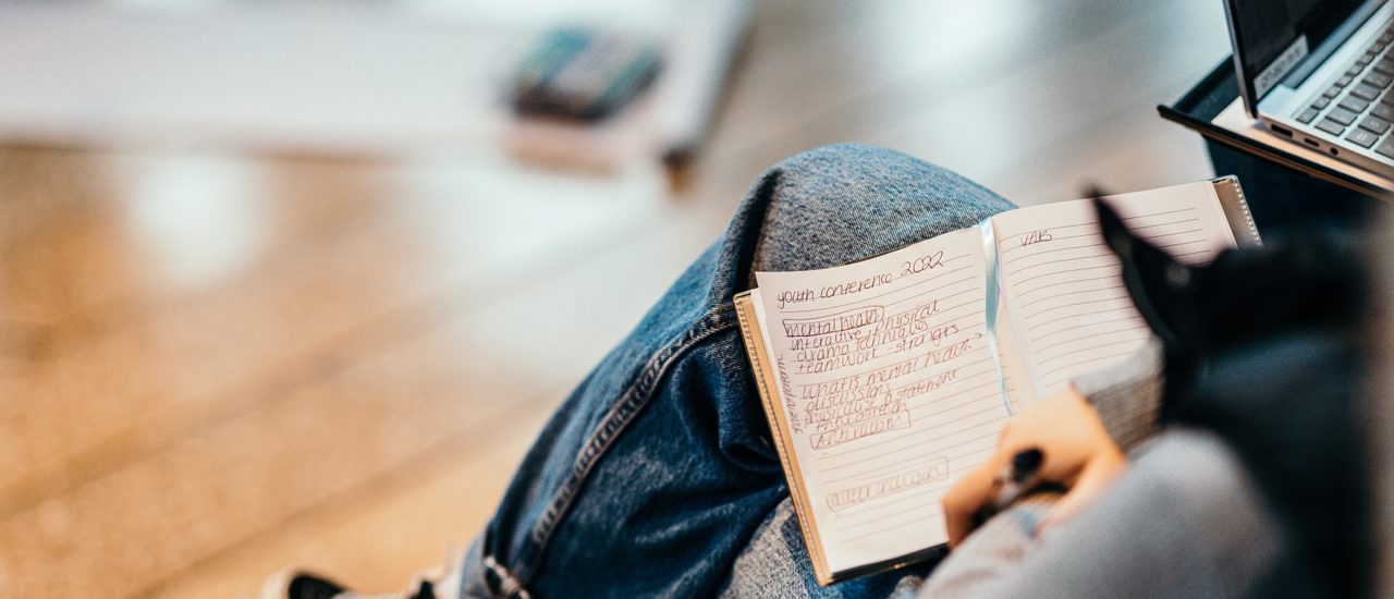 Person wearing jeans sitting down with an open notebook and pen in their lap.