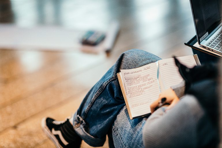 Person wearing jeans sitting down with an open notebook and pen in their lap.