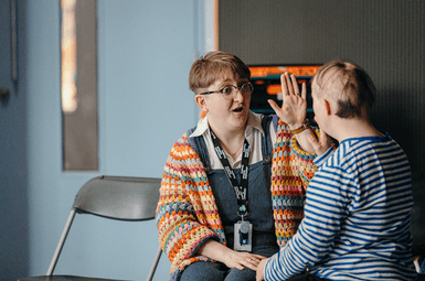A Lady with a CFT lanyard in a colourful cardigan is high fiving a lady wearing a navy and white striped top