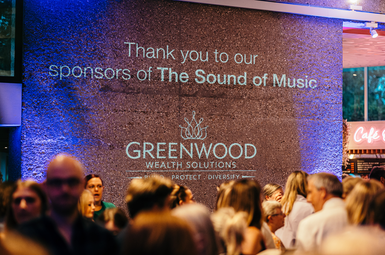 A projection with busy crowds below, the projection reads thank you to our sponsor of the sound of music