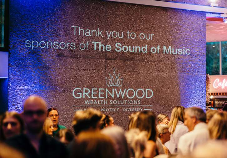 A projection with busy crowds below, the projection reads thank you to our sponsor of the sound of music