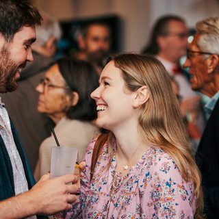 A group of people gather in a CFT Foyer; a young man and woman smile and laugh.