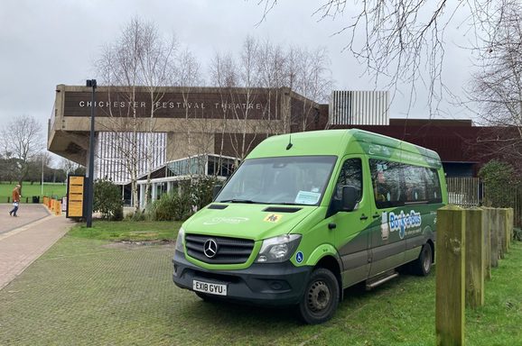 A green bus is parked outside the Festival Theatre on a grey cloudy day.