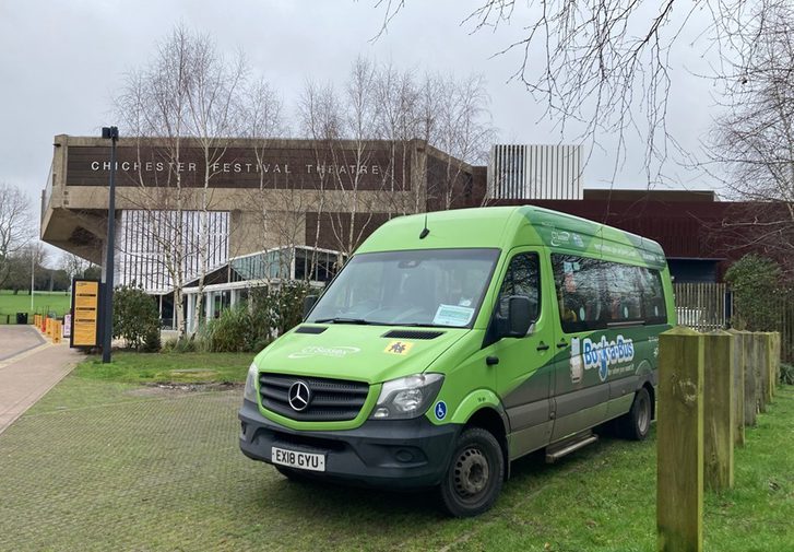 A green bus is parked outside the Festival Theatre on a grey cloudy day.
