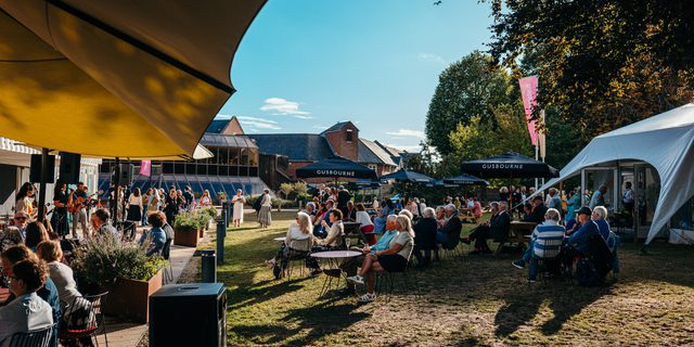 People sit outside in the sunny park beside the Festival Theatre