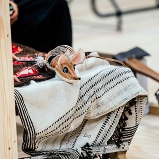 A small, brown mouse puppet is resting on a pile of blankets.